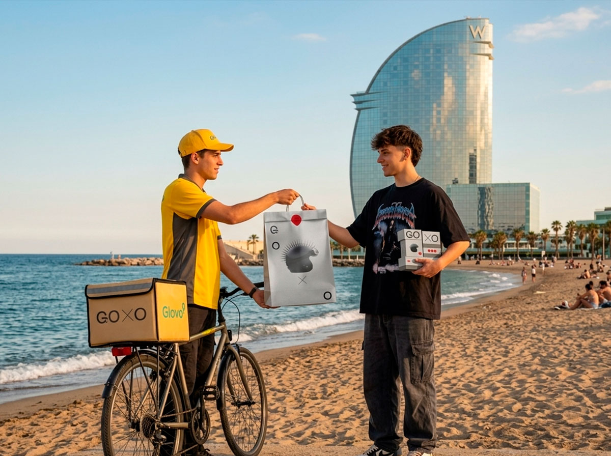 Repartidor de Glovo entregando un delivery gourmet en Barcelona a un chico en la playa de Barcelona frente al Hotel W de Barcelona.